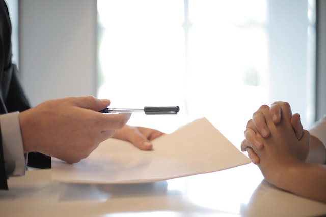 Cropped person handing a white sheet and a pen to someone else